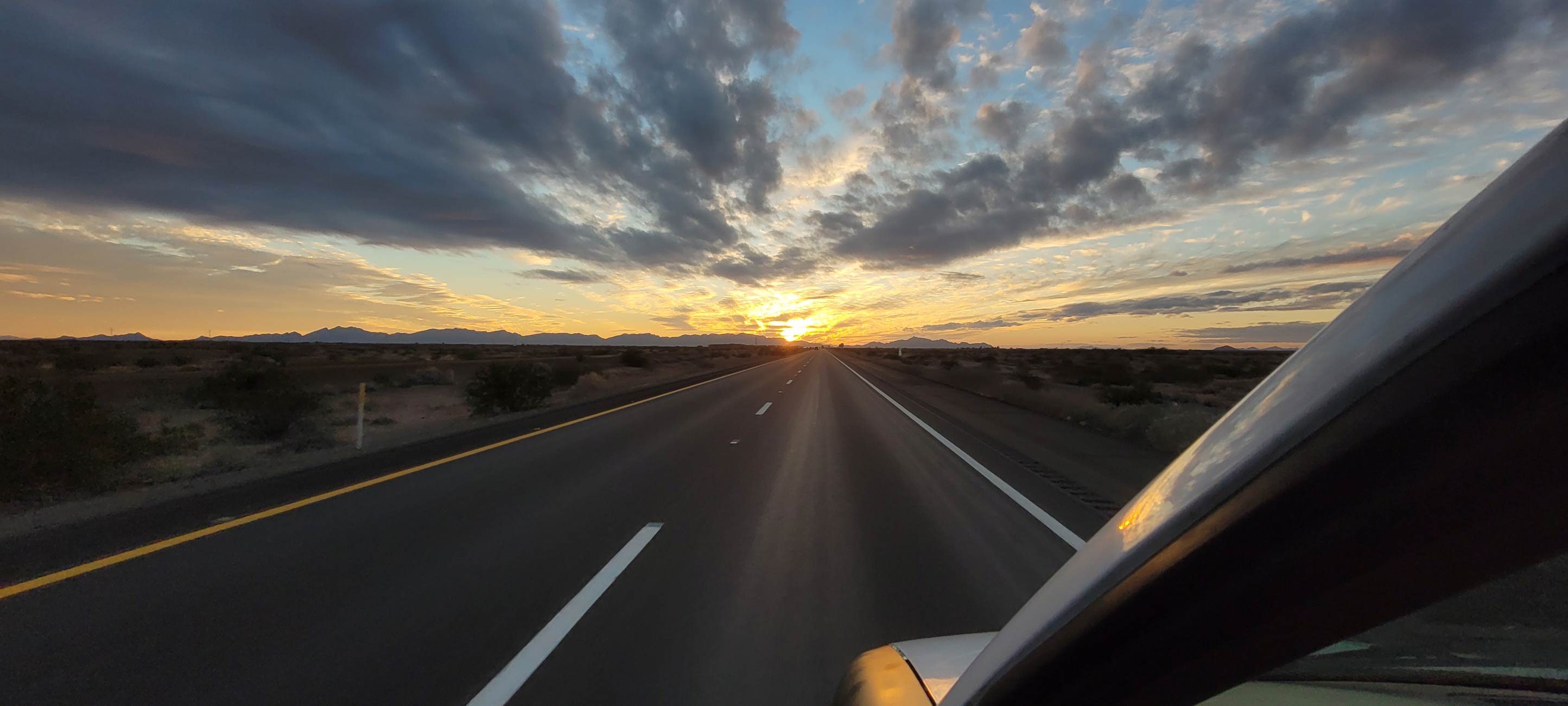 Out On The Open Road - Photo of Road Extending All the Way to a Setting Sun Mountainaous Landscape with Colorful Clouds